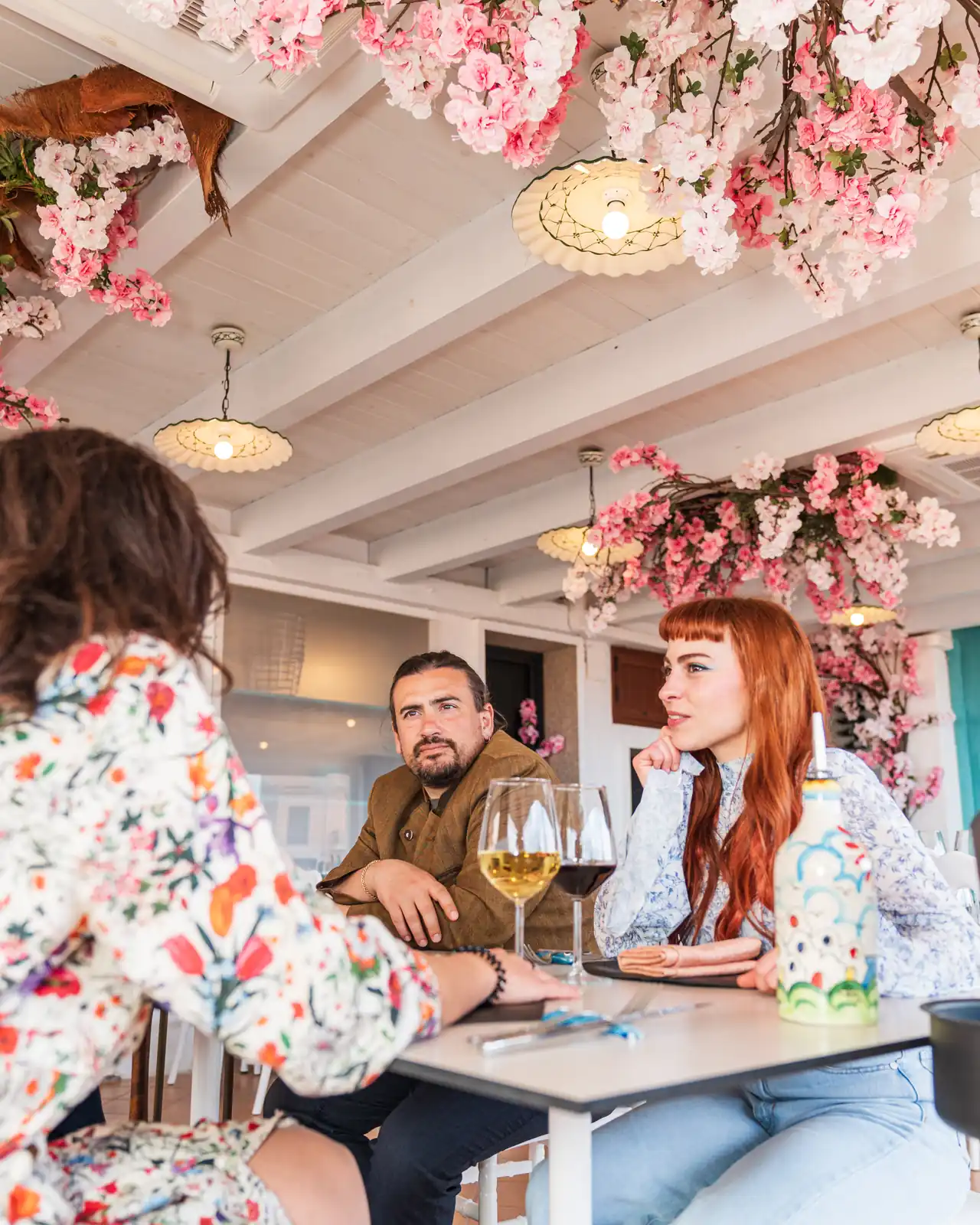 Zwei Gäste am Tisch unter den Blumen, mit einem Glas Wein