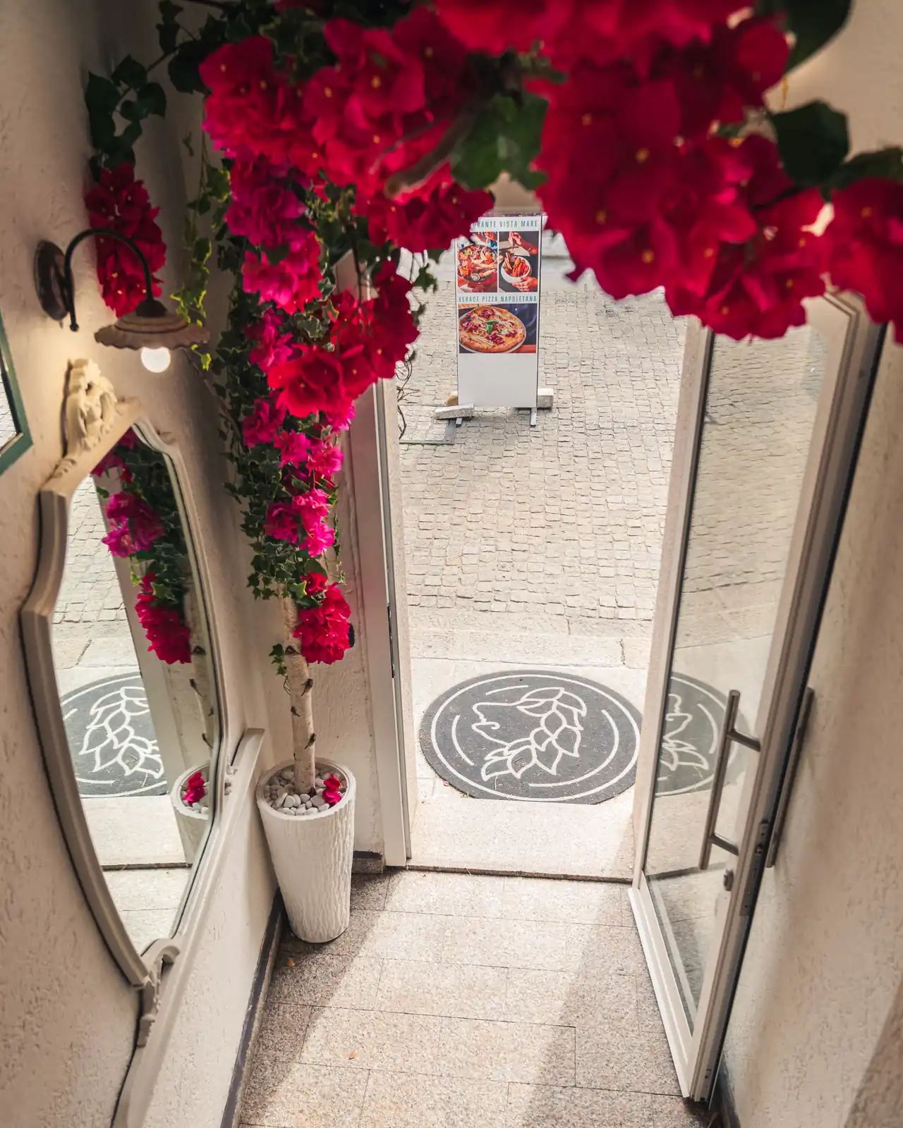 Der Eingang des Restaurants mit der Bougainvillea und dem Logo auf dem Boden