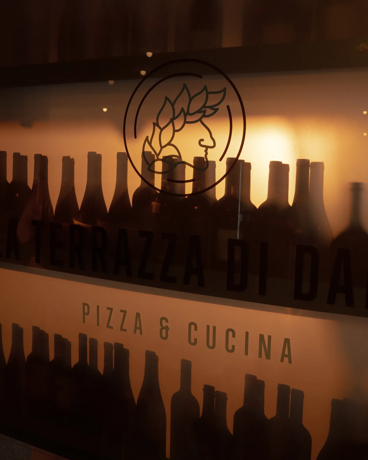 Il logo de La Terrazza di Dante inciso sulla vetrata, con le bottiglie di vino dietro