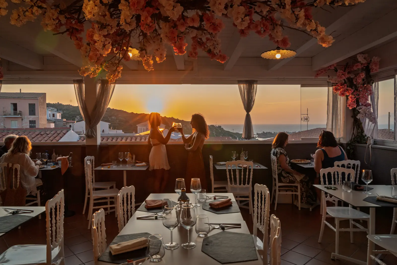 Die Terrasse bei Sonnenuntergang mit Gästen an den Tischen und Vorhängen im Wind